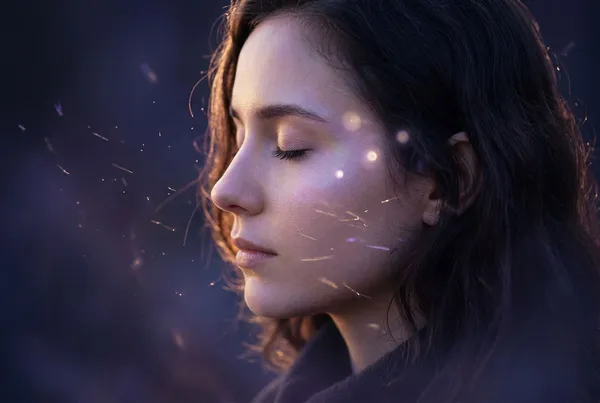 側面半身女子站在夜晚森林邊緣，周圍環繞著細碎光粒，遠方樹間透出柔和金光，深靛藍夜色與暖光交織，人物輪廓清晰而寧靜