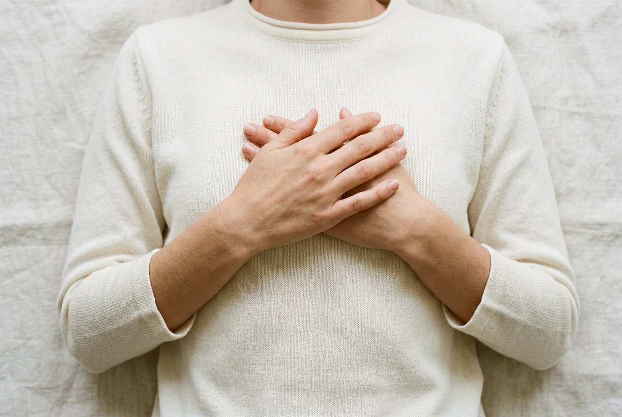 空中俯視兩隻手交疊放在胸口，身穿米白色衣物，光線柔和均勻，胸口向下的構圖，兩側留有大量空間